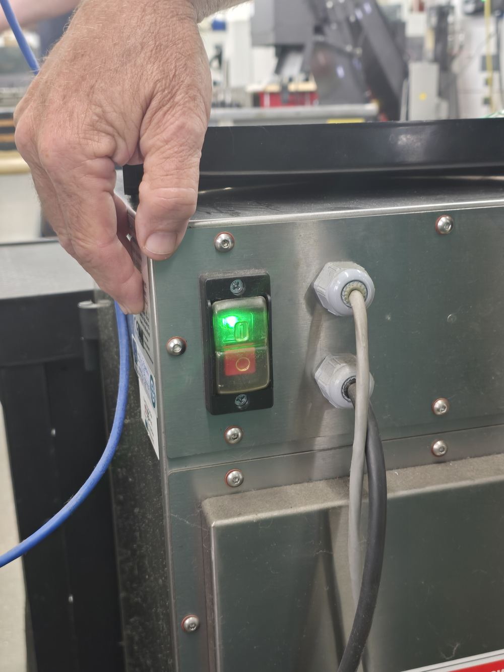 Illuminated I/O rocker switch on the stainless side panel of the fume extractor cabinet, green I segment lit, a hand reaching toward it.