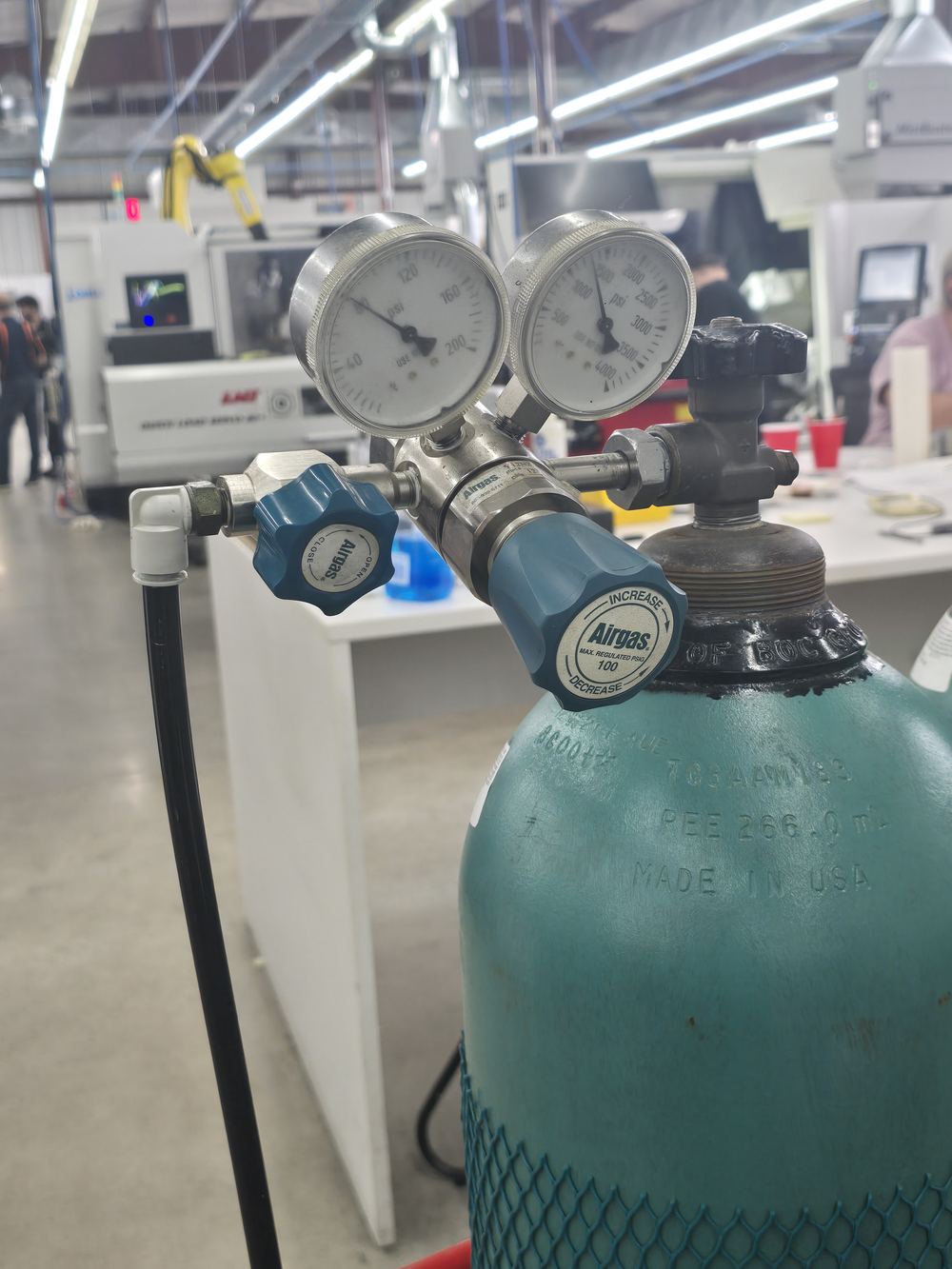 A teal high-pressure nitrogen cylinder in a rack behind the cell, two-stage regulator fitted.