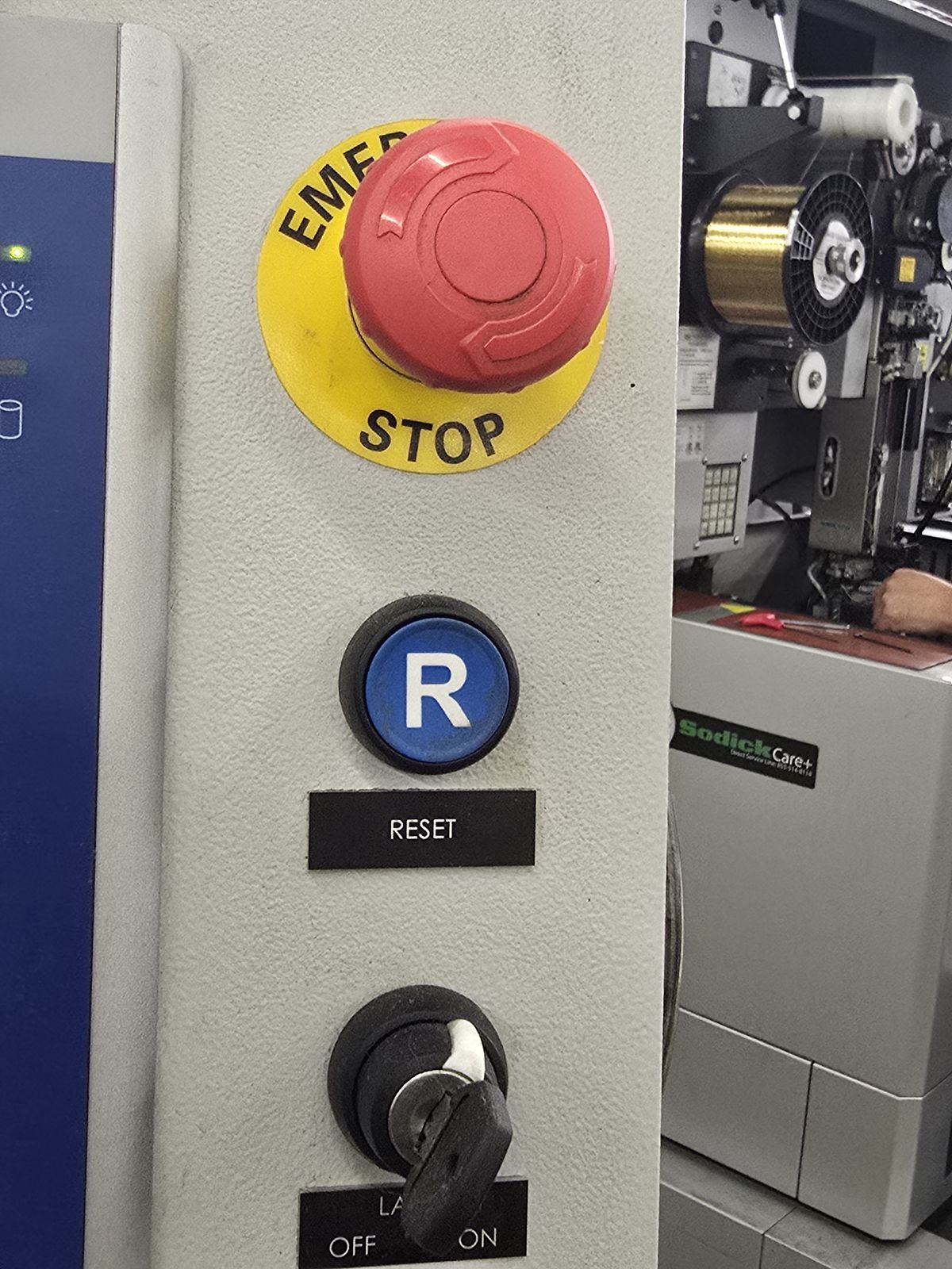 The physical operator control column: red EMERGENCY STOP mushroom on a yellow disc, a blue button carrying a white letter R with a RESET legend beside it, and the LASER OFF/ON key switch.