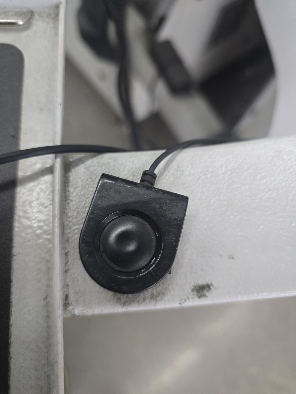 An unlabelled corded pushbutton on the edge of the keyboard shelf at the operator station.